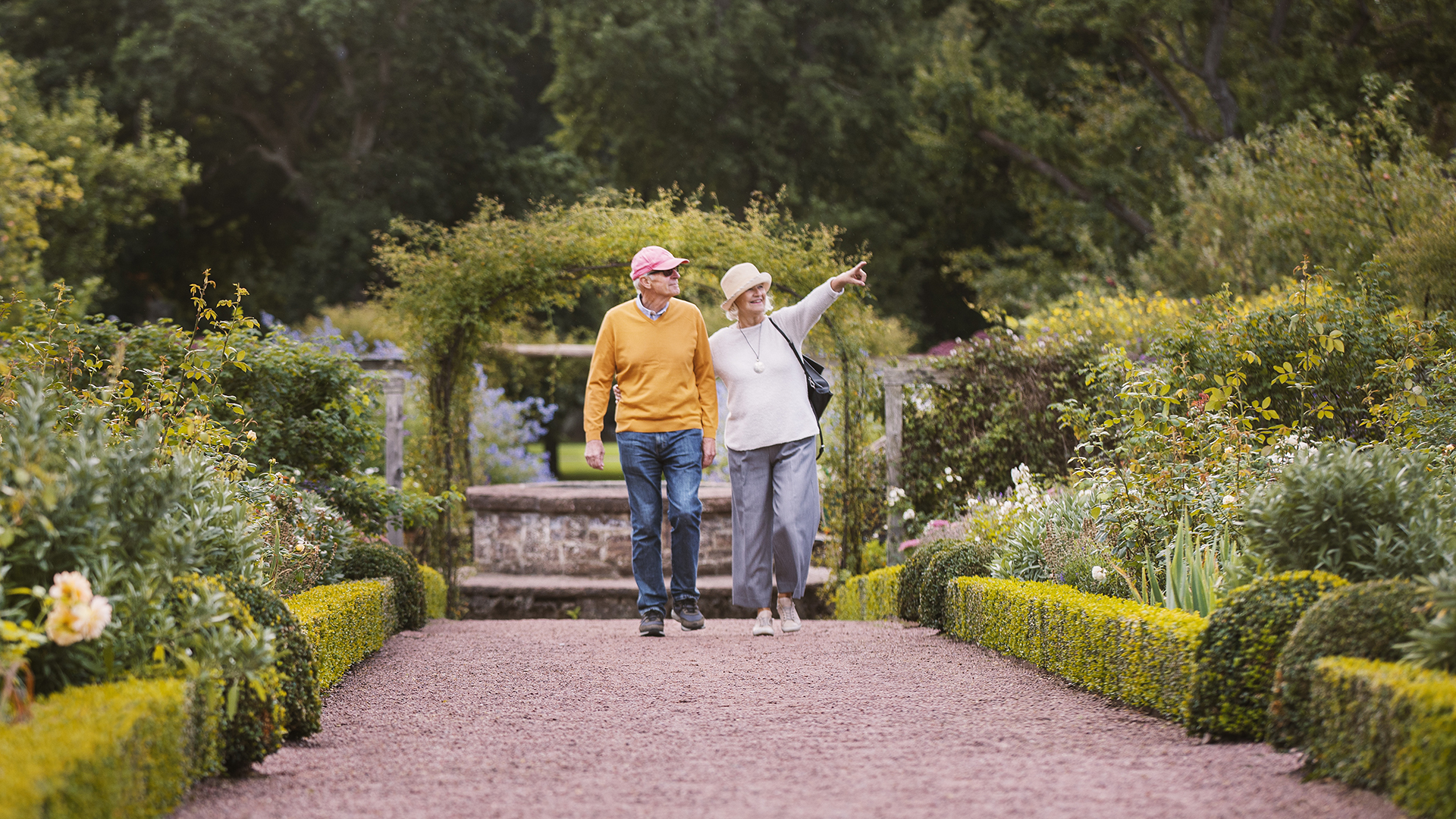Äldre par som promenerar i trädgård.