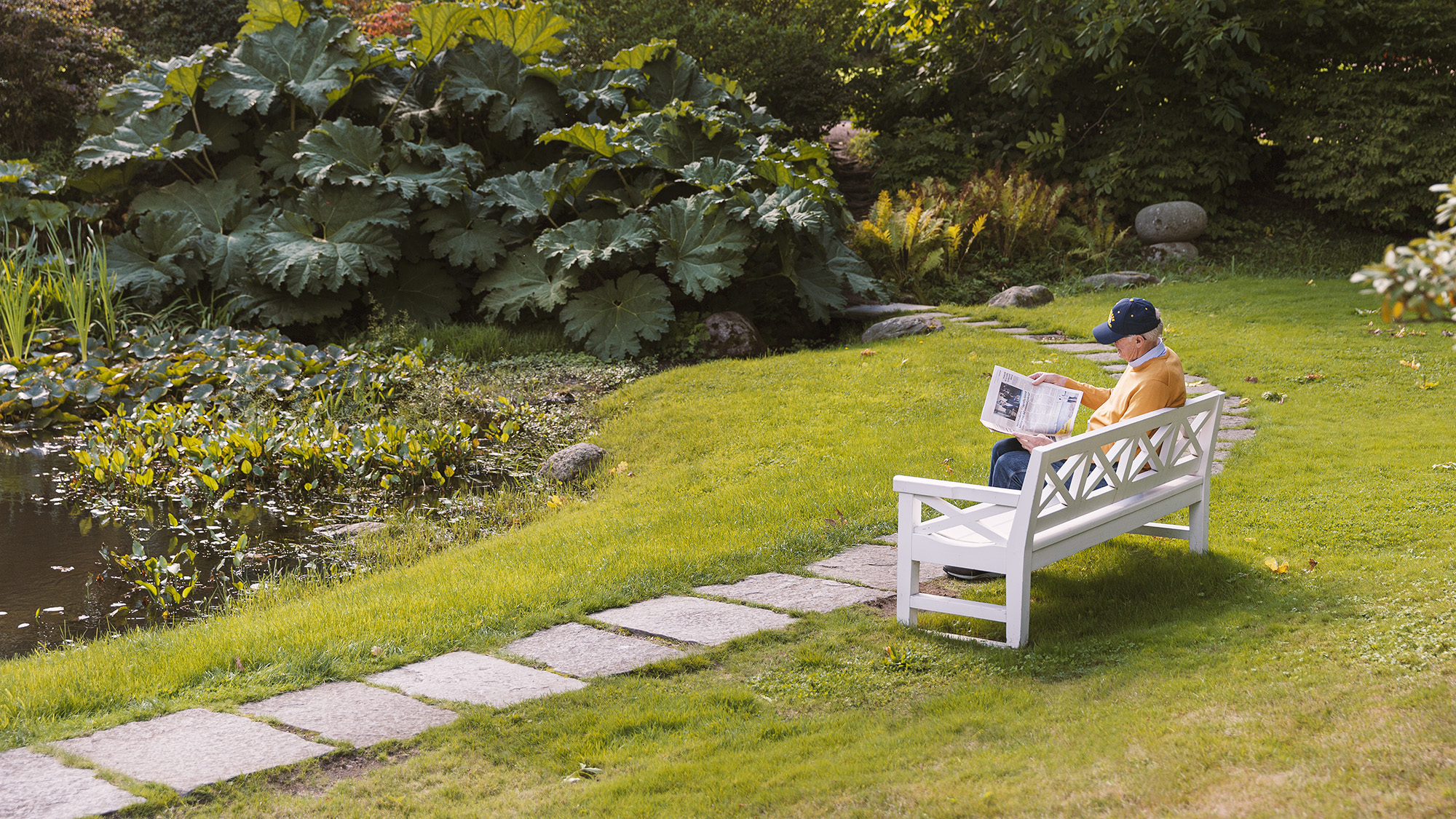 Man på parkbänk läser tidning.